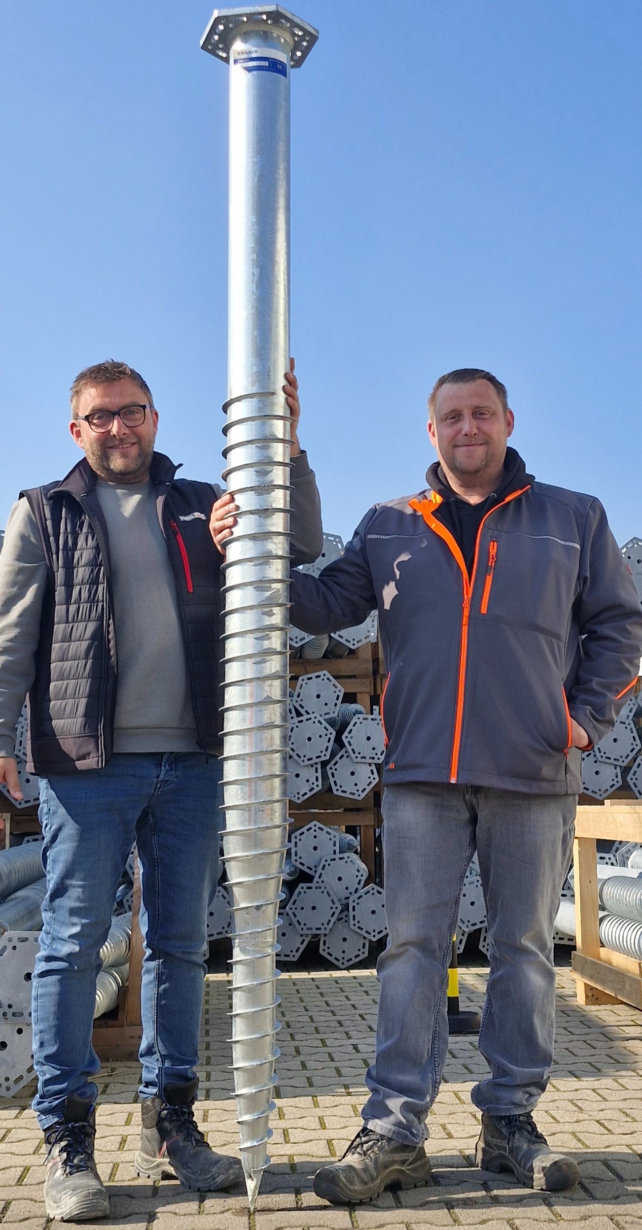 Brüder Thiel halten ein Riesenschraubfundament in den Händen.